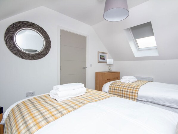 A bedroom with two beds, a round mirror, a wooden cabinet, and a skylight.