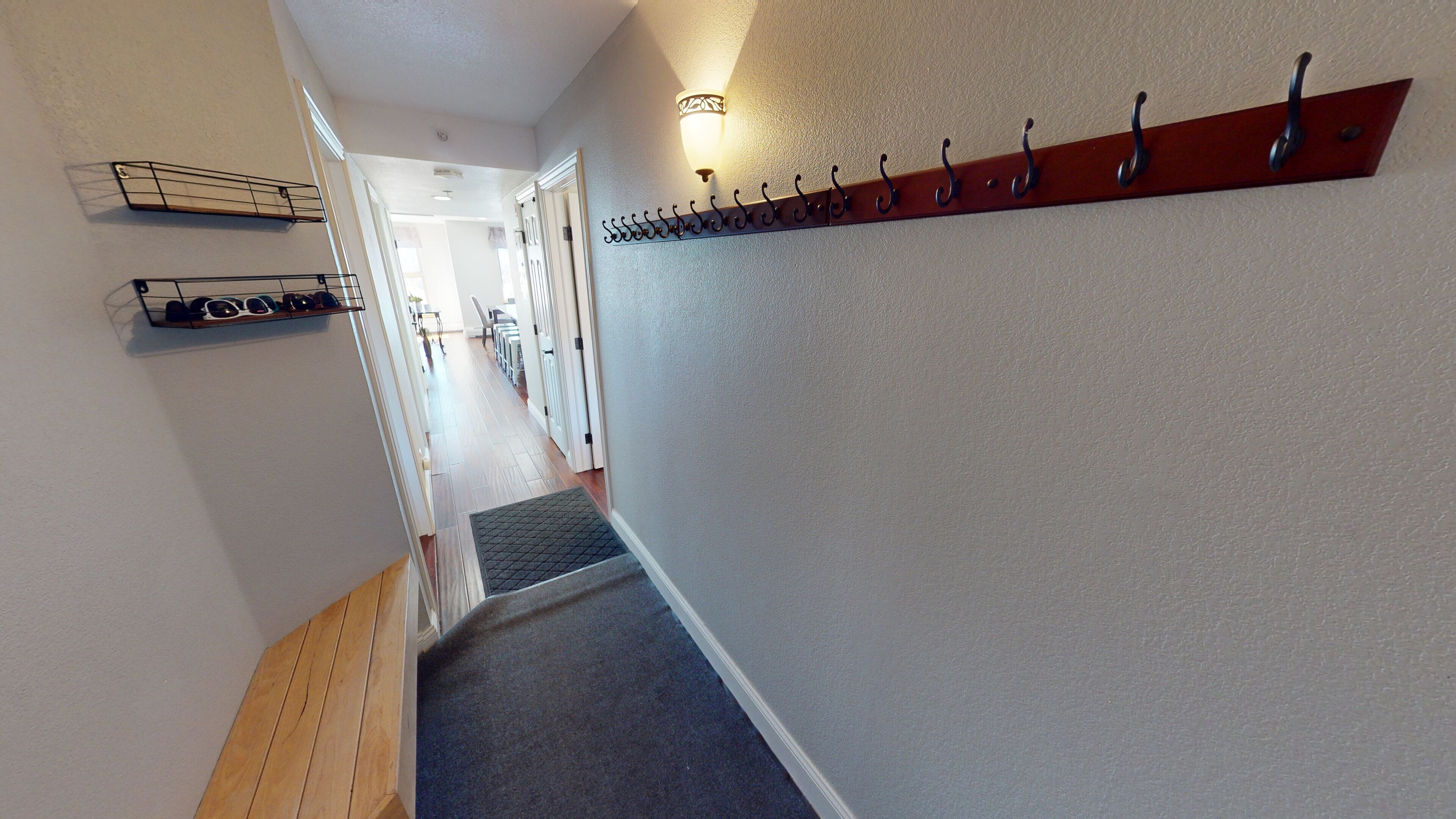 Un couloir doté d’un plancher en bois, d’un porte-manteau et d’un luminaire fixé au mur.