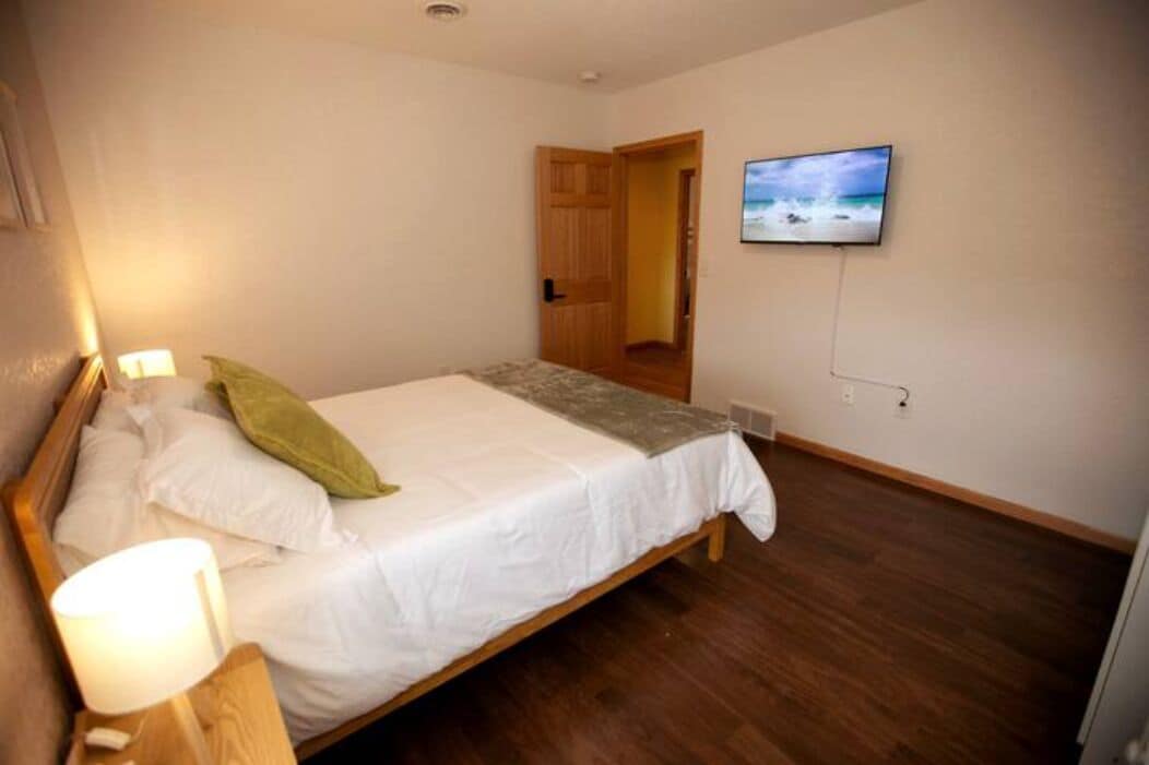 Ein Schlafzimmer mit einem Bett, einem an der Wand montierten Fernseher und Holzboden.