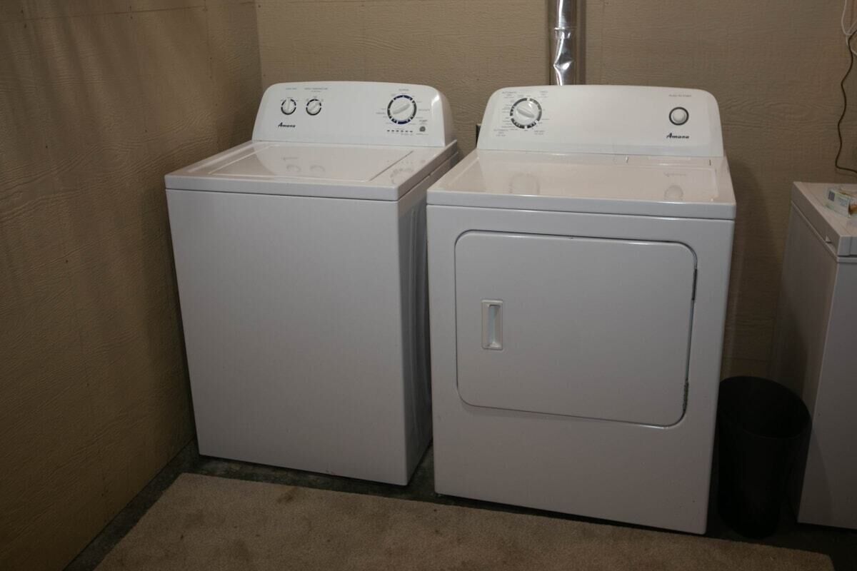 Una sala de bugaderia amb dues rentadores blanques de càrrega frontal i una màquina d'assecar.