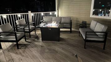 An outdoor patio with a fire feature, seating, and a view of the city at night.