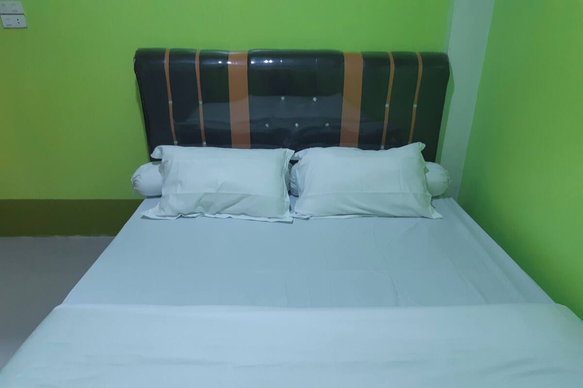 A bed with a headboard, two pillows, and a white bedspread in a room with green walls.