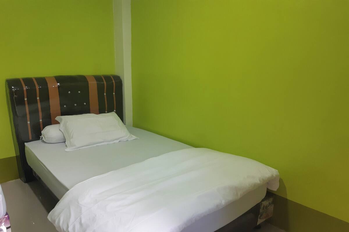 A single bed with a striped headboard and white bedding in a room with green walls.