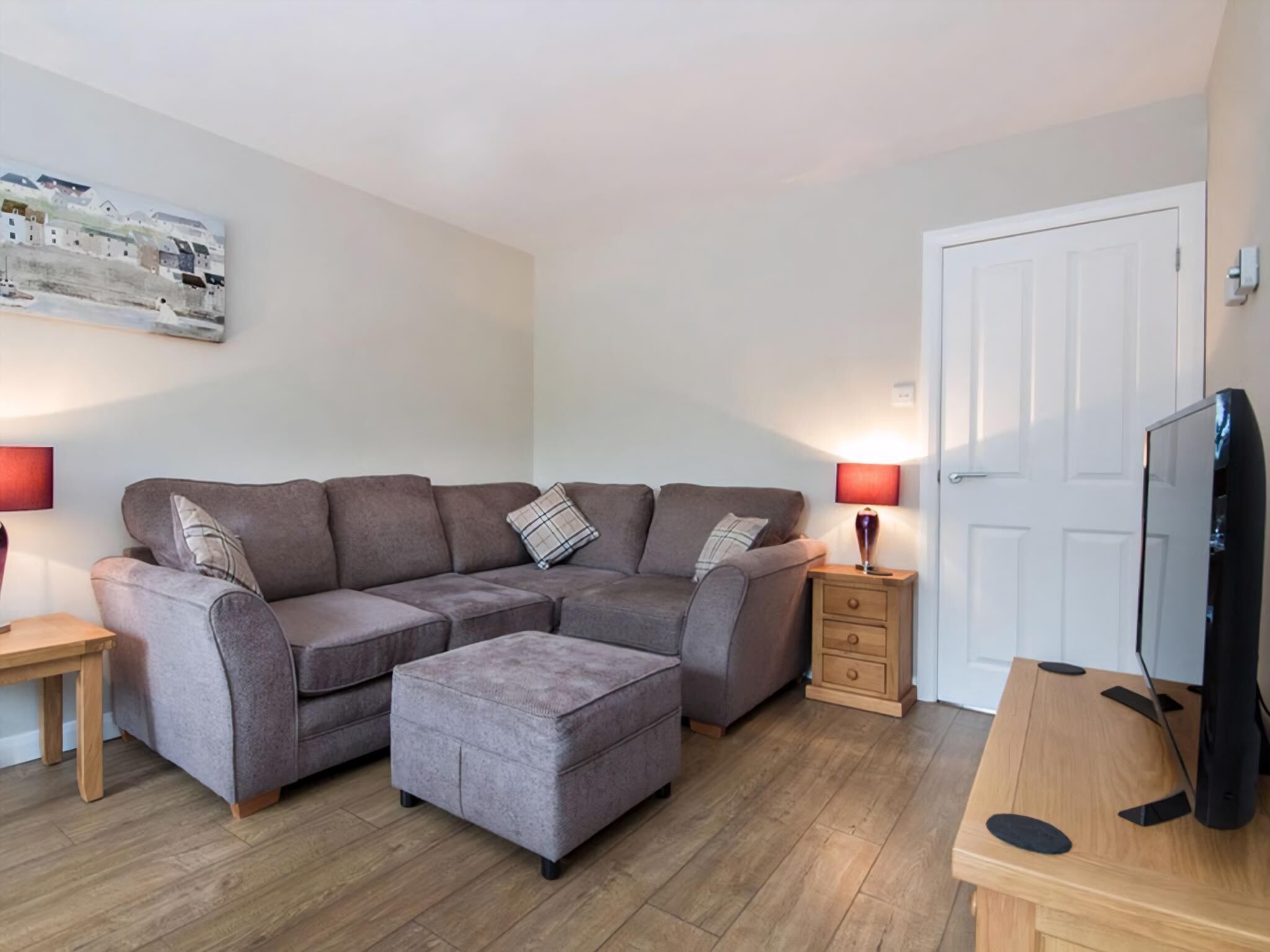 A modern living room with a grey sectional sofa, a wooden coffee table, and a television on a wooden stand.