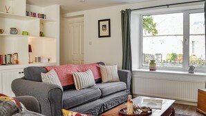 A living room with a grey sofa, a coffee table with a tray, a bookshelf, and a window with curtains.