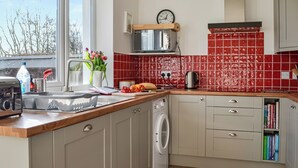 A kitchen with a washing machine, a toaster, a kettle, and a clock on the wall.