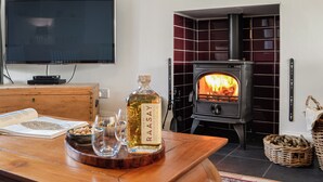 A living room with a television, a wooden table with a bottle, glasses, and a book, and a wood-burning stove.