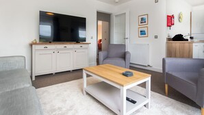 A modern living room with a flat-screen TV, a wooden coffee table, and grey armchairs.