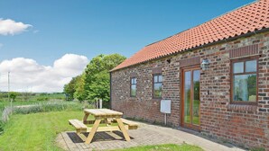 A brick building with a red-tiled roof, a wooden picnic table, and a grassy area.
