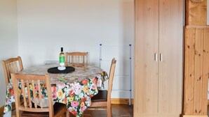 A dining area with a round table covered by a floral tablecloth, wooden chairs, a bottle of wine, and a clock on a wooden cabinet.