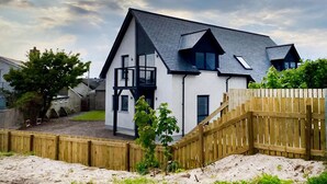 A modern two-story house with a balcony, a wooden fence, and a sandy yard. - Amazing coastal location with access to sandy beach. (Balintore, near Tain)