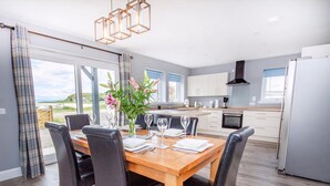 A modern kitchen with white cabinets, a central island, and a dining area with a wooden table and black chairs. - Amazing coastal location with access to sandy beach. (Balintore, near Tain)