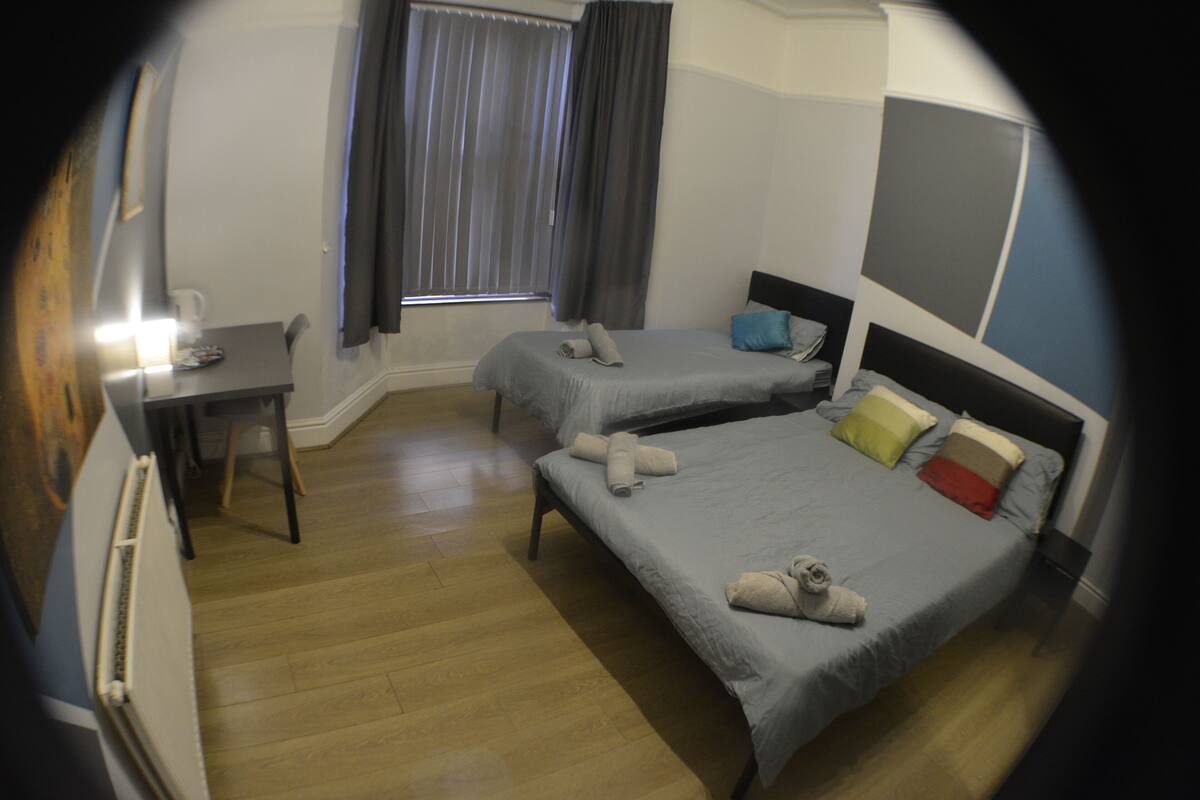A hotel room with two single beds, a desk, and a window with curtains.