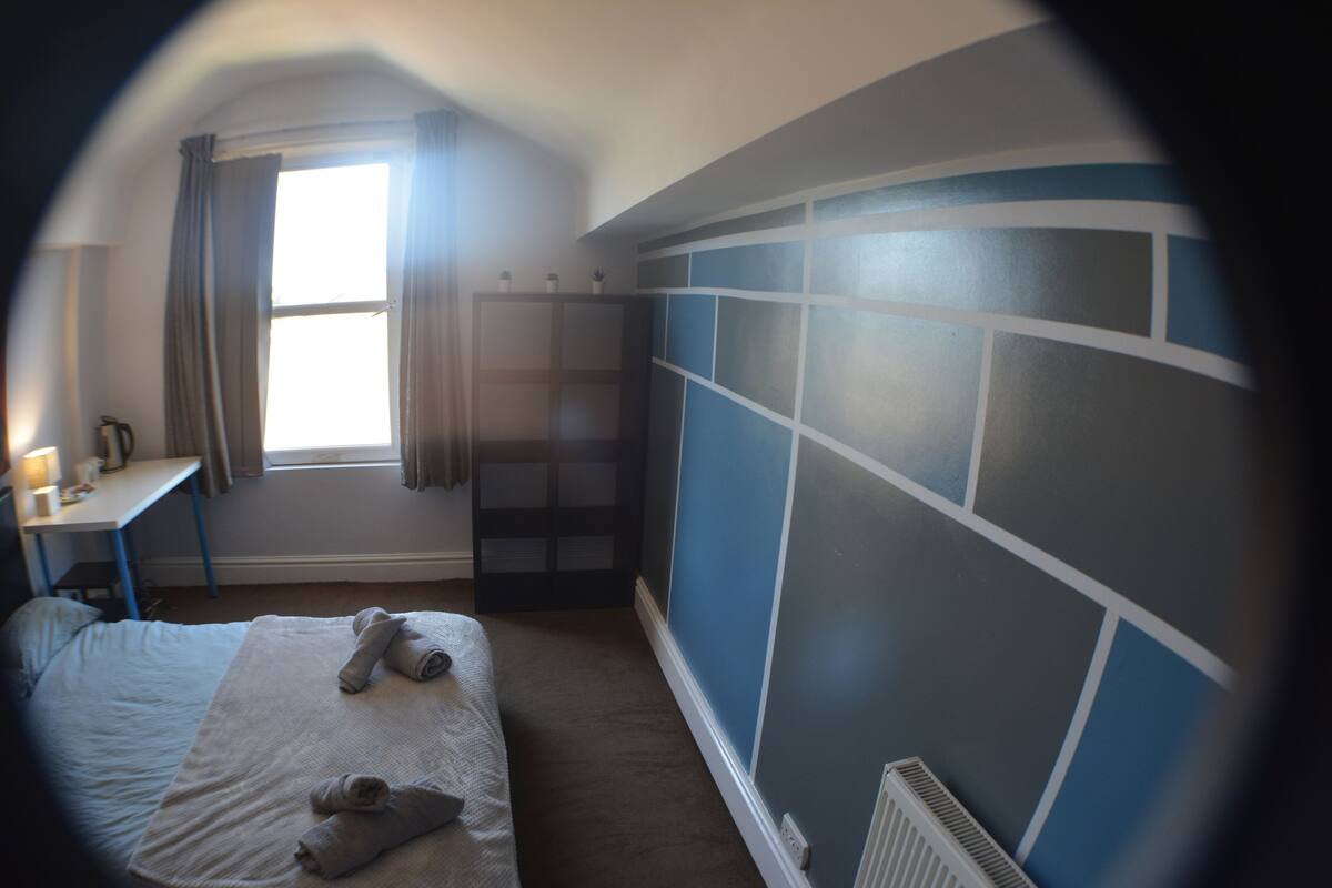 A bedroom with a bed, a desk, a window, and a radiator.