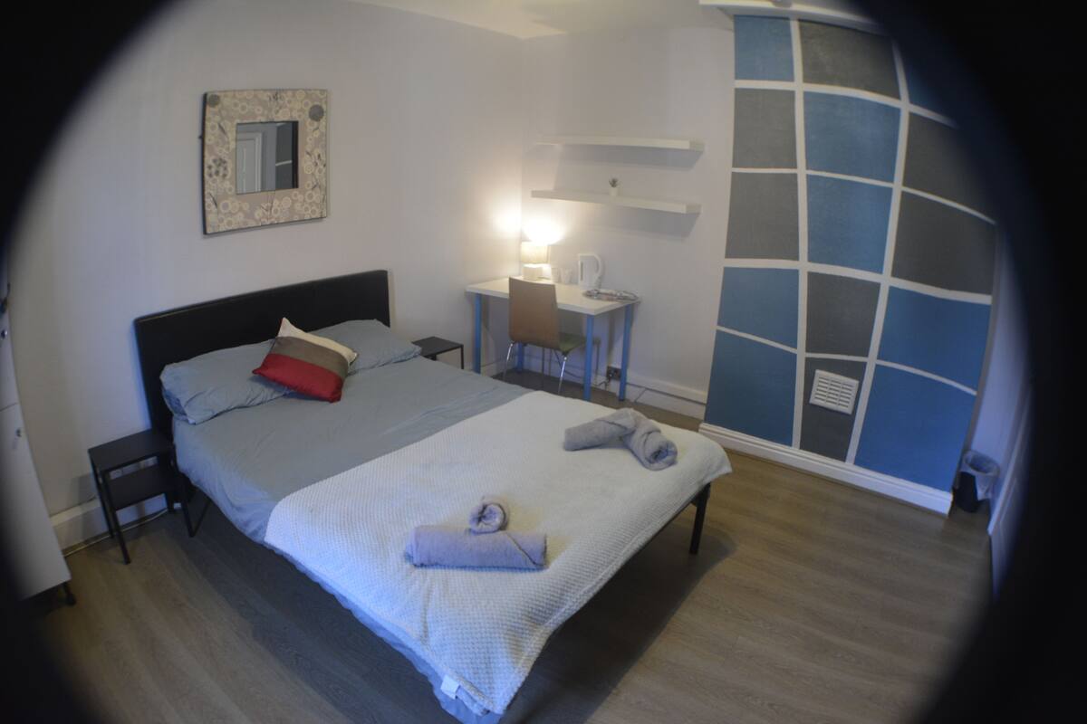 A neatly arranged bedroom with a bed, bedside table, and a desk with a chair.