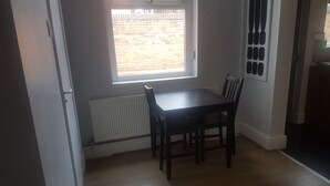 A room with a dining table and chairs, a window with a view of a brick wall, and a radiator. - Kensington Guest House Liverpool (Liverpool)