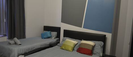 A hotel room with two beds, each with a headboard, grey bedding, and rolled towels.