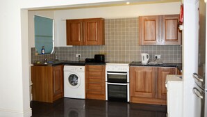 A compact kitchen with wooden cabinets, a washing machine, an oven, and a refrigerator. - Kensington Guest House Liverpool (Liverpool)