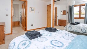 A bedroom with a bed, a dresser, a mirror, and a door leading to a bathroom. - 3 bedroom accommodation in Dornoch (Dornoch)