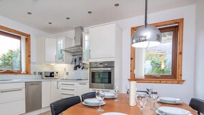 A modern kitchen with white cabinets, a dining table set for six, and a large window with a view of greenery. - 3 bedroom accommodation in Dornoch (Dornoch)