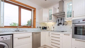 A modern kitchen with white cabinets, a built-in dishwasher, a stainless steel oven, and a window with a wooden frame. - 3 bedroom accommodation in Dornoch (Dornoch)