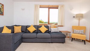 A living room with a grey sectional sofa, a yellow armchair, and a small table. - 3 bedroom accommodation in Dornoch (Dornoch)