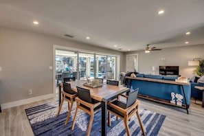 A modern kitchen with a blue countertop, a dining area with a wooden table and chairs, and a large sliding glass door leading to a patio area.
