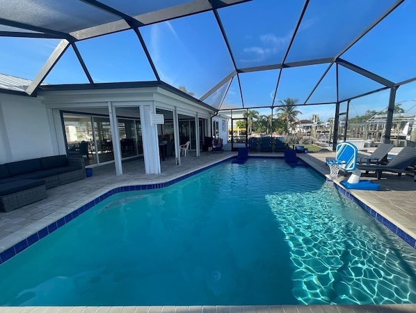 An indoor swimming pool with a glass ceiling, lounge chairs, and a basketball hoop.