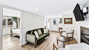 Un salon moderne avec un canapé vert, deux fauteuils, une petite table ronde et un téléviseur fixé au mur.
