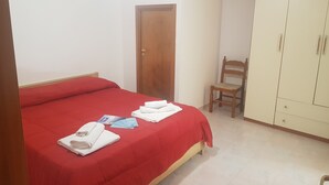 A bedroom with a red bedspread, a wooden door, a wooden chair, and a wardrobe. - Trilocale Ulivo Baia Verde piano terra (Gallipoli)