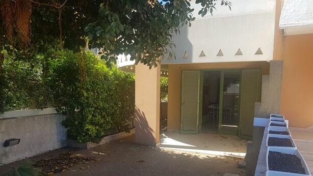 A narrow alleyway with a brick pathway, a concrete wall, and a row of white planters with soil. - Trilocale Ulivo Baia Verde piano terra (Gallipoli)