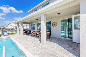 Ein modernes Haus mit überdachter Terrasse, Schwimmbad und Essbereich.