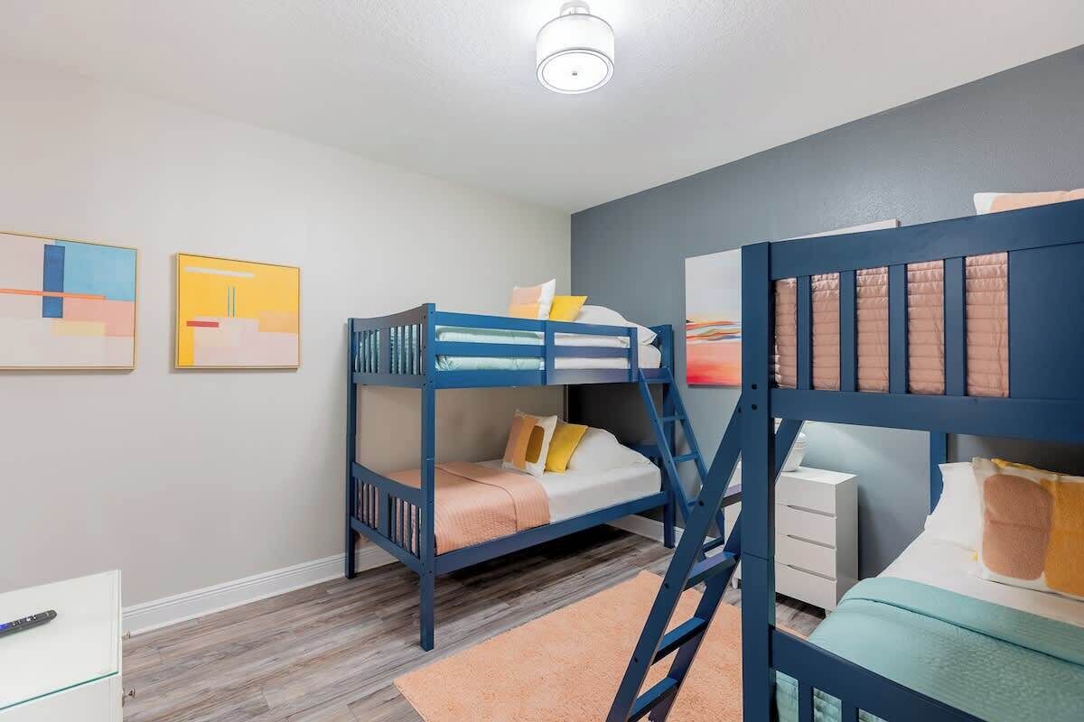 Een kamer met twee stapelbedden, een witte ladekast en abstracte wanddecoratie.