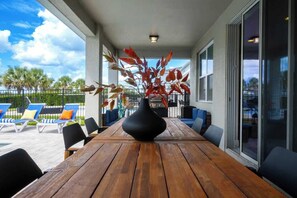 Ein Holztisch mit einer schwarzen Vase in der Mitte, umgeben von Stühlen, auf einem Balkon mit Blick auf Palmen und einen klaren Himmel.