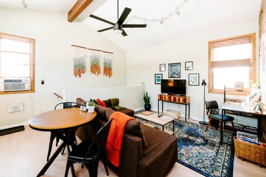 A living room with a wooden dining table, brown sofa, and a ceiling fan.