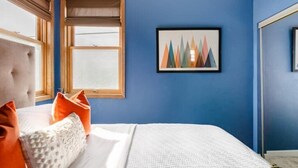 A bedroom with a large bed, a window with blinds, and a framed picture on the wall.