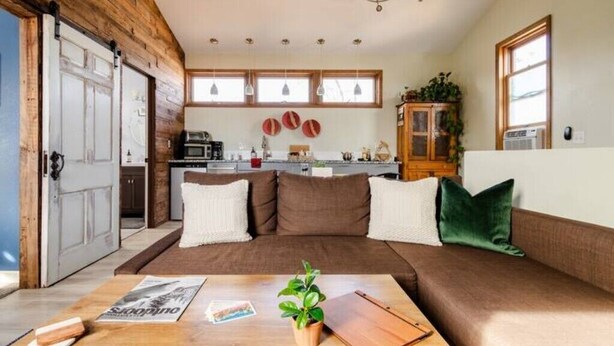 A cozy living room with a brown sofa, a wooden coffee table, and a kitchen in the background.