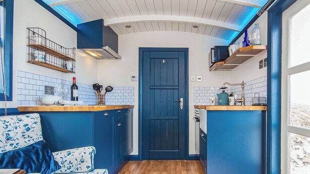A compact kitchen with blue cabinetry, a wooden countertop, and a blue door.