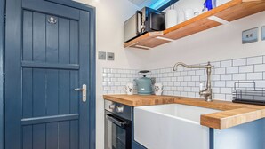 A modern kitchen with a blue door, white tiled backsplash, wooden countertop, stainless steel appliances, and a built-in oven.