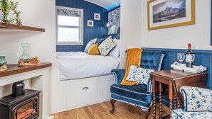 A cozy room with a bed, a blue armchair, a wooden table, and a fireplace.