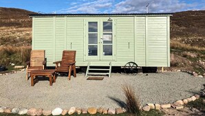 A small, single-story building with a green exterior and a window. There are two wooden chairs and a small table in front of the building.