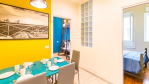 A dining area with a blue table set for four, a painting on the wall, and a staircase leading to another room. - Central Station Apts by Wonderful Italy - Cetara (Naples)