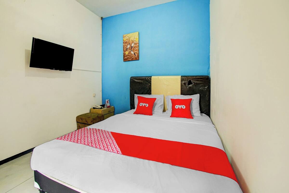 A hotel room with a bed, a flat-screen TV mounted on the wall, and a painting above the bed.
