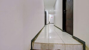 Un largo pasillo estrecho con pisos y paredes de baldosas blancas, que conduce a una puerta de madera oscura al final.