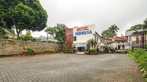 Entrada de un hotel con un camino pavimentado, un muro de piedra y un gran letrero que dice "HOTEL NIRWANA".