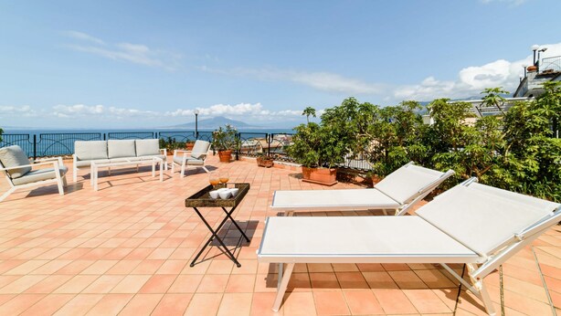 Terraza en la azotea con sillones blancos, una pequeña mesa con bebidas y plantas en macetas.