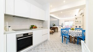 Una cocina moderna con armarios blancos, horno empotrado y comedor con sillas azules y una mesa.