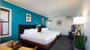 A hotel room with two beds, a desk, a chair, a potted plant, and artwork on the walls. - Classic Retro Motel in Bozeman (Bozeman)