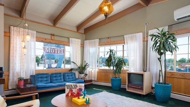 A motel room with a blue sofa, a round coffee table with toys, a TV, and large windows with curtains. - Classic Retro Motel in Bozeman (Bozeman)