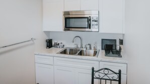 A compact kitchen with white cabinets, a stainless steel microwave, a double sink, and a small countertop area with a coffee maker and utensils. - Classic Retro Motel in Bozeman (Bozeman)